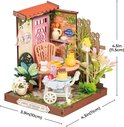 Miniatuur theeservies in een tuin met roze deur, bakstenen muur en bloemen. Afmetingen 11.5x10x11cm.