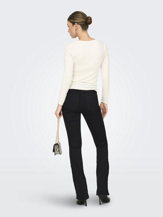 Model in zwarte flared jeans, wit shirt, witte blazer en zilveren tasje.