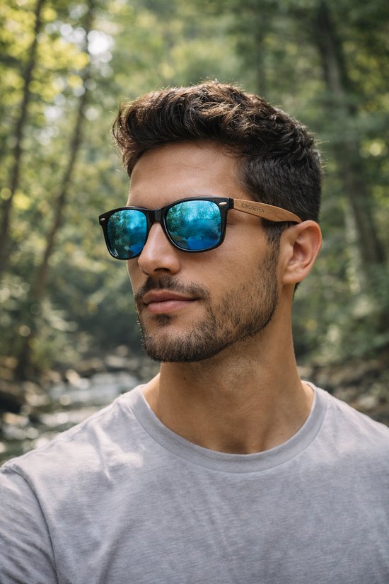 Man met zwarte zonnebril met houten pootjes, blauwe spiegelglazen en een grijze T-shirt, bos op achtergrond.