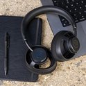 Zwarte JLab open-ear koptelefoon ligt op een zwart notitieboek naast een laptop.