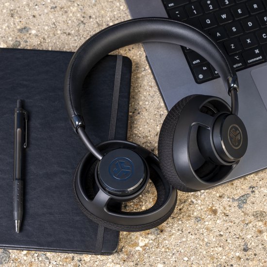 Zwarte JLab open-ear koptelefoon ligt op een zwart notitieboek naast een laptop.