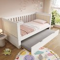 Wit slaapbank met uittrekbaar bed, roze dekens, gestreept kussen en lamp.