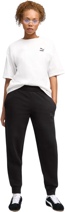 Model draagt een zwarte Puma joggingbroek met elastische tailleband en logo op linkerbeen, gecombineerd met witte T-shirt.