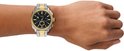 Gouden en zilverkleurig Fossil horloge om een pols met donkere huidskleur.