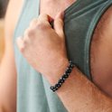 Man draagt een groene tanktop en een dubbele rij armband met zwarte en grijze kralen om zijn pols.