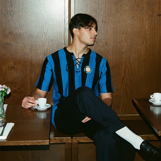 Jonge man in blauw-zwart gestreept retro voetbalshirt met vetersluiting, zittend aan tafel.