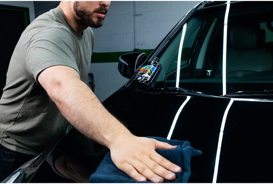 Een man met een grijze t-shirt poetst de motorkap van een zwarte auto met een donkere microvezeldoek.