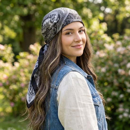 Een vrouw met lang bruin haar draagt een zwart-witte paisley bandana, een denim vest en een wit shirt.