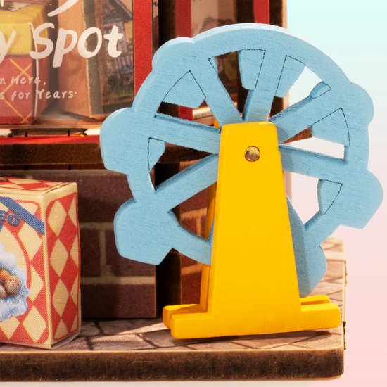 Close-up van een miniatuur blauwe reuzenrad met gele standaard, naast een speelgoedwinkel.
