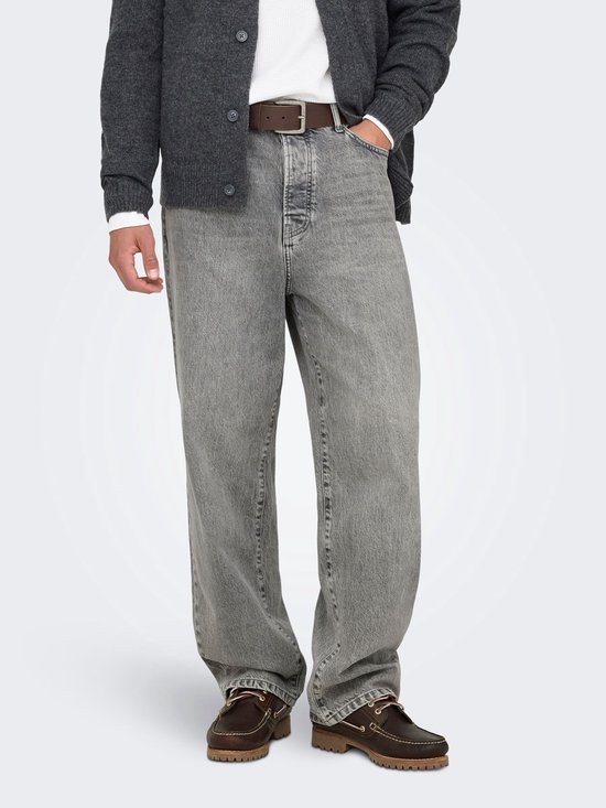 Een man draagt een grijze jeans met rechte pijpen, een grijze vest en bruine instappers.