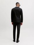 Man in zwart colbert en broek, van achteren gezien, met zonnebril.