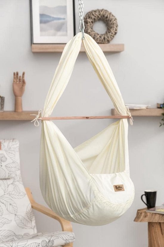 Roomwitte babyhangmat hangend aan een ketting, met houten spreider.
