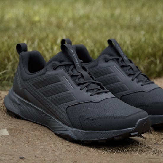 Paar zwarte Adidas Terrex trailrunningschoenen op een ondergrond van zand en gras.