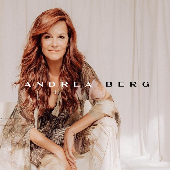 Andrea Berg met lang rood haar, zittend in een beige outfit met grafische print.