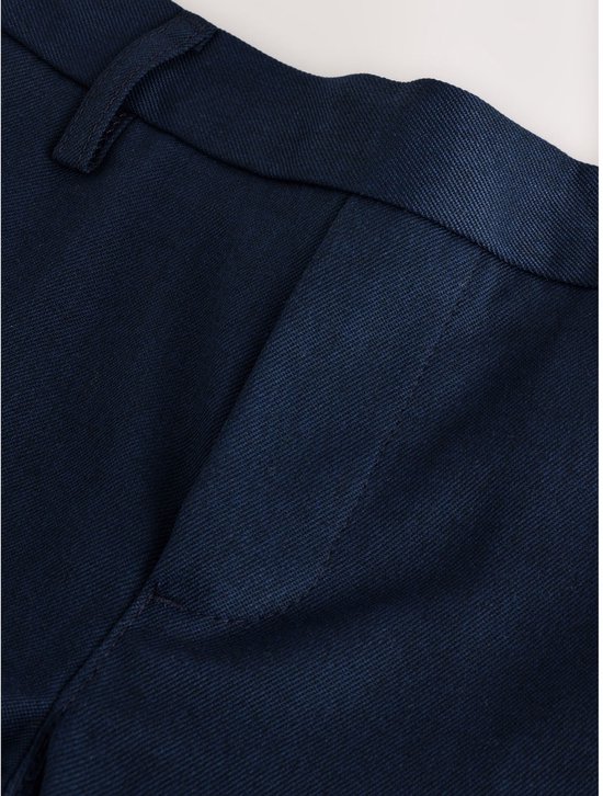Sluiting van een donkerblauwe broek met ceintuurlussen, knopen en een steekzak.
