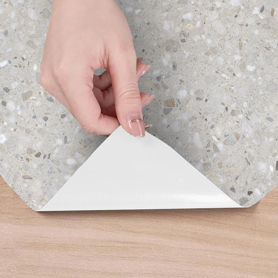 Hand die een hoek van de grijze terrazzo zelfklevende vloerbedekking optilt.