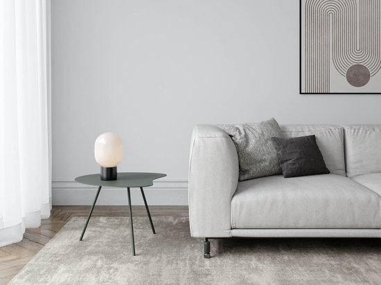 Une table d'appoint organique vert Rosemary avec trois pieds élancés, à côté d'un canapé gris avec des coussins.