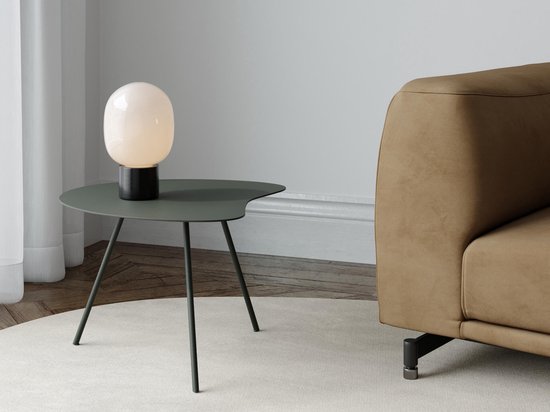 Une table d'appoint organique ronde vert Rosemary avec trois pieds élancés, à côté d'un canapé marron et d'une lampe.