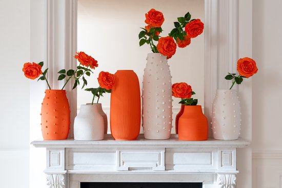 Zes vazen met oranje rozen op een schouw. Twee grote witte met stippen, een oranje met ribbels, een kleine oranje, een kleine witte met stippen, een middelgrote oranje.