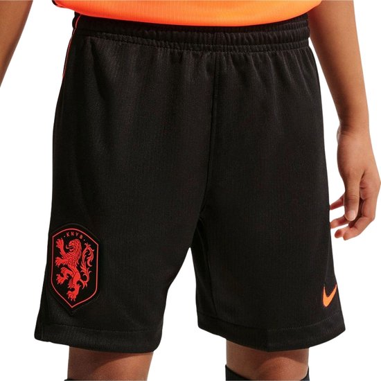 Onderlichaam van meisje in oranje shirt en zwarte korte broek met oranje KNVB-wapen en Nike logo.
