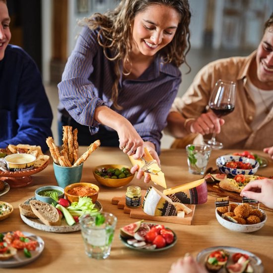 Vrouwen snijden kaas op een tafel vol met hapjes en drankjes.