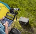 Donkergrijs Jackery Explorer 500 powerstation met oranje accenten, aangesloten naast een laptop met een groep zebra's op het scherm, bij een tent.