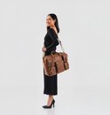 Vrouw met zwarte kleding draagt een bruine leren laptoptas over haar schouder.