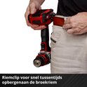 Een man gebruikt een rode en zwarte Einhell accuboormachine in een werkplaats. De boormachine is vastgeklikt aan zijn riem.