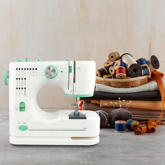 Witte Rynix naaimachine met groene accenten, naast een mand met spoelen en stoffen.