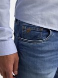 Close-up van de rechterzak van een spijkerbroek in lichtblauw denim, met een oranje P-logo.