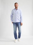 Man in het midden van een lichtblauwe gestreepte blouse en een lichtblauwe spijkerbroek, met witte sneakers. Bekeken vanaf de voorkant.