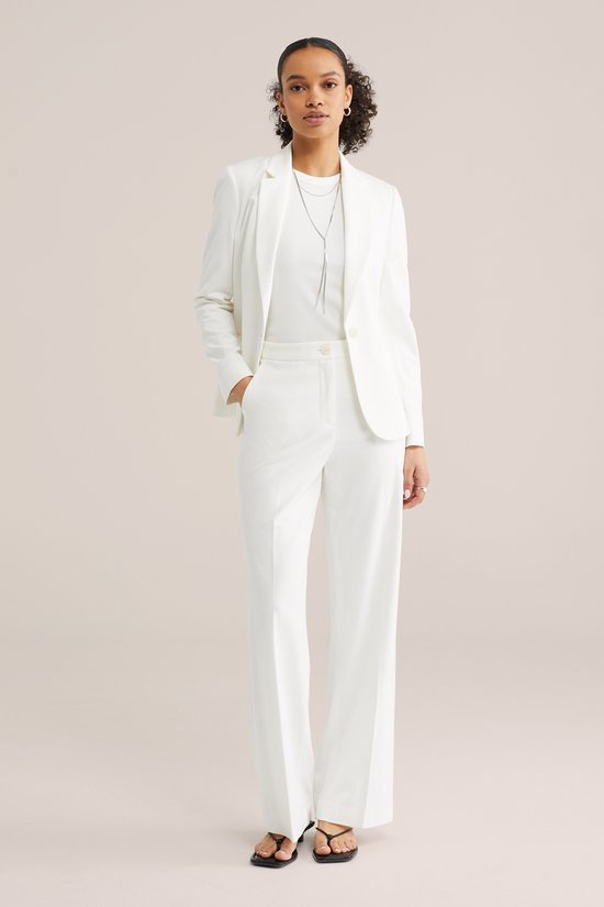 Model draagt witte getailleerde blazer met bijpassende witte wijde broek en een witte top.