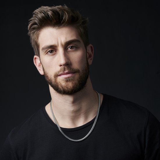 Close-up van een man met een zwarte t-shirt die een zilverkleurige schakelketting draagt.