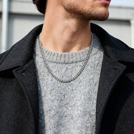 Close-up van een man die een zilverkleurige schakelketting draagt over een grijze trui.