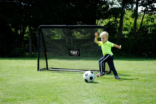 Jongetje met groen shirt en donkere broek schiet op zwart EXIT voetbaldoel.