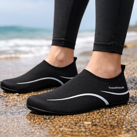 Zwarte Travelhawk waterschoenen op een strand met kiezels en water.