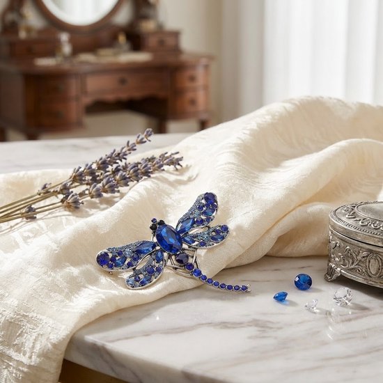 Blauwe libelle broche met zilverkleurig metaal en fonkelende facet geslepen stenen op een crèmekleurige sjaal.