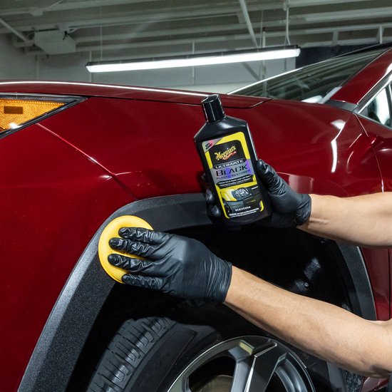 Hand in zwarte handschoen brengt Meguiar's Ultimate Black aan op zwarte kunststof wielkast van rode auto.