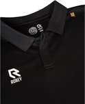 Detail van de kraag van een zwarte poloshirt met het 'Robey Racket Club' logo en een klein goudkleurig klavertje.
