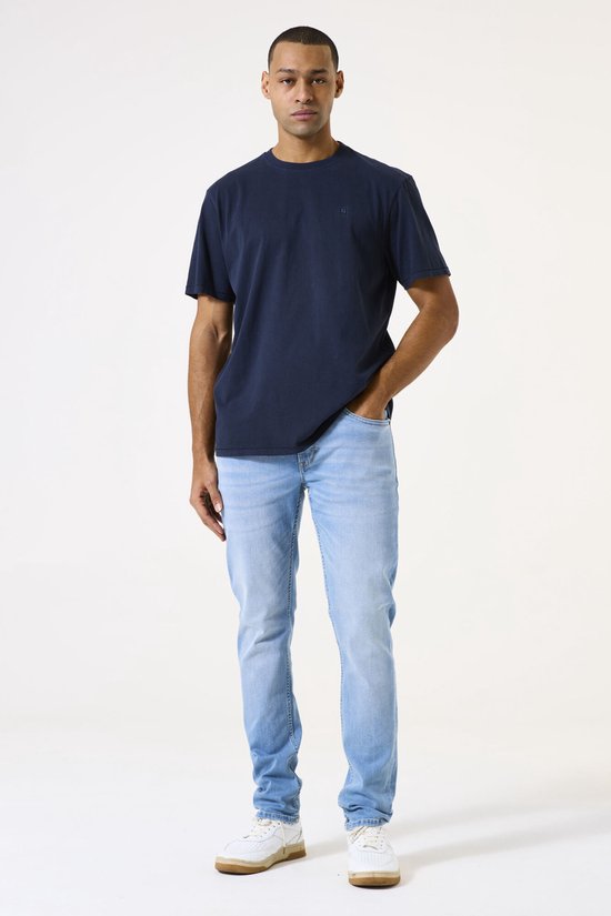Man met donkere huid in een donkerblauw T-shirt en lichtblauwe spijkerbroek.