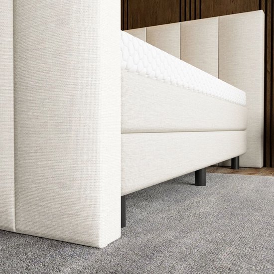 Close-up van de beige boxspring met een gestreept hoofdbord en een matras met honingraatpatroon.