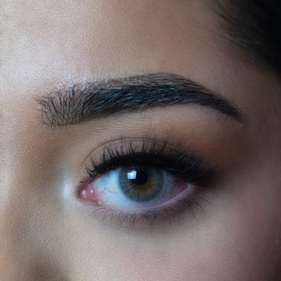 Extreem close-up van een vrouwenoog dat een grijze contactlens met een lichte oogirritatie toont.