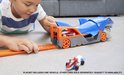 Jongen speelt met blauwe Hot Wheels haaienauto transporteur op de vloer, laadt een rode auto.
