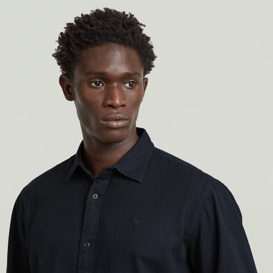 Man, van dichtbij, draagt een donkerblauw regular fit overhemd, model met kraag en knopen.