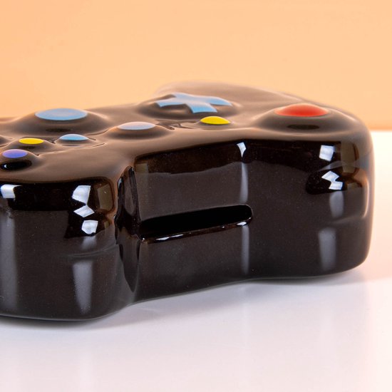 Tirelire noire en céramique en forme de manette de jeu, avec boutons colorés et une fente pour les pièces.