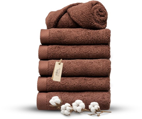 Stapel bruine Miss Towels handdoeken op zwarte achtergrond met een label en katoenbloemen.