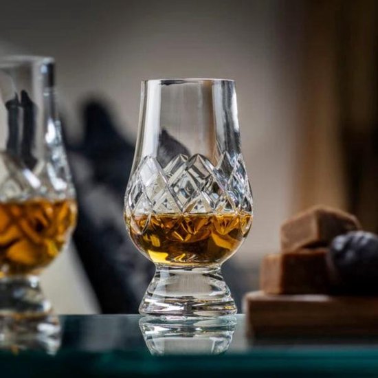 Een kristallen whiskyglas met ruitpatroon, gevuld met amberkleurige whisky. Een ander glas is deels zichtbaar.