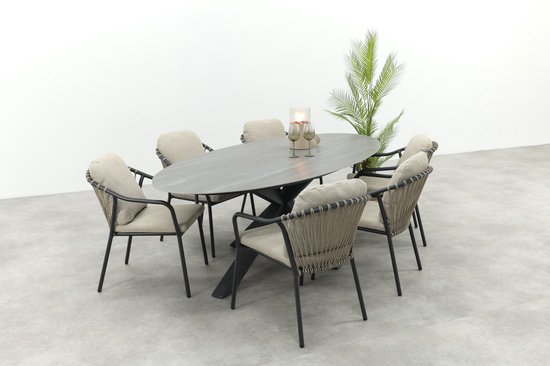Ovaal steenkleurig tafelblad met zes beige tuinstoelen en op de achtergrond een plant.