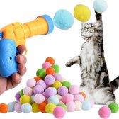 Een grijze cyperse kat vangt een bal uit de lucht, met een stapel gekleurde pompons en een geel/blauw schietpistool.