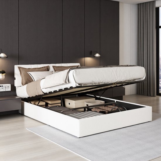 Wit tweepersoonsbed met opklapbaar matras en opbergruimte voor kleding en koffers.